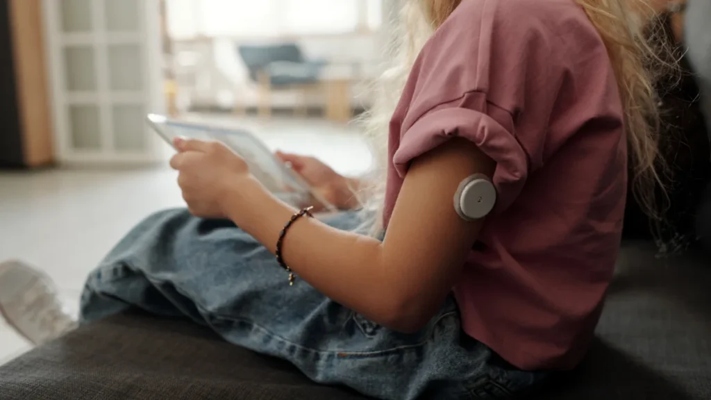 Menina com sensor de glicose no braço usando um tablet