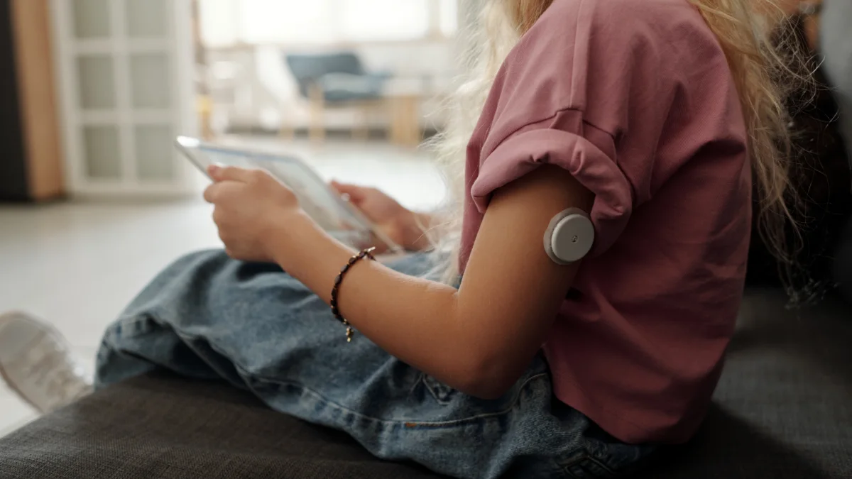 Menina com sensor de glicose no braço usando um tablet