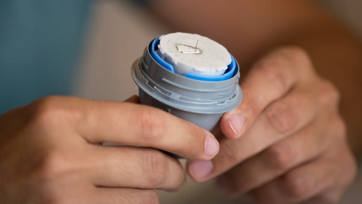 Sensor de glicose sendo segurado entre os dedos, em close