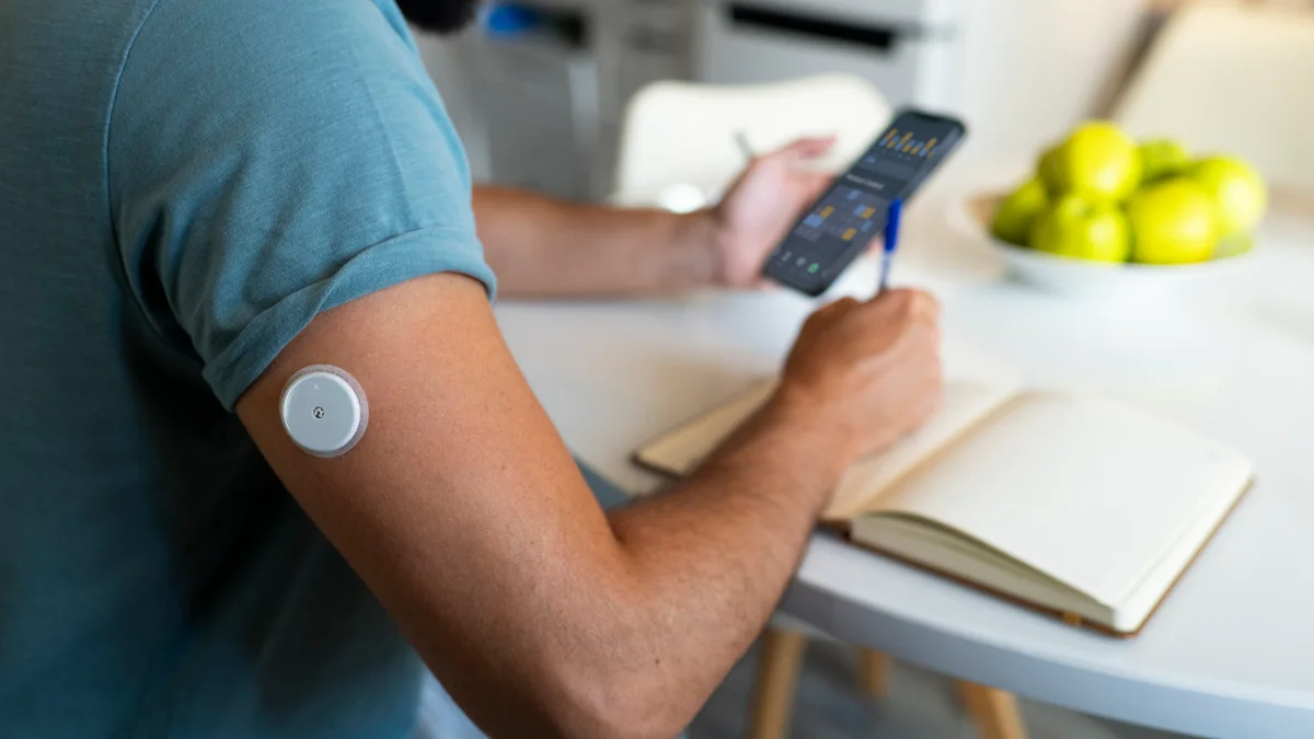 Homem com sensor de glicose no braço consultando o celular à mesa