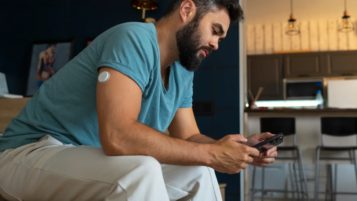 Homem com sensor de glicose no braço olhando o celular