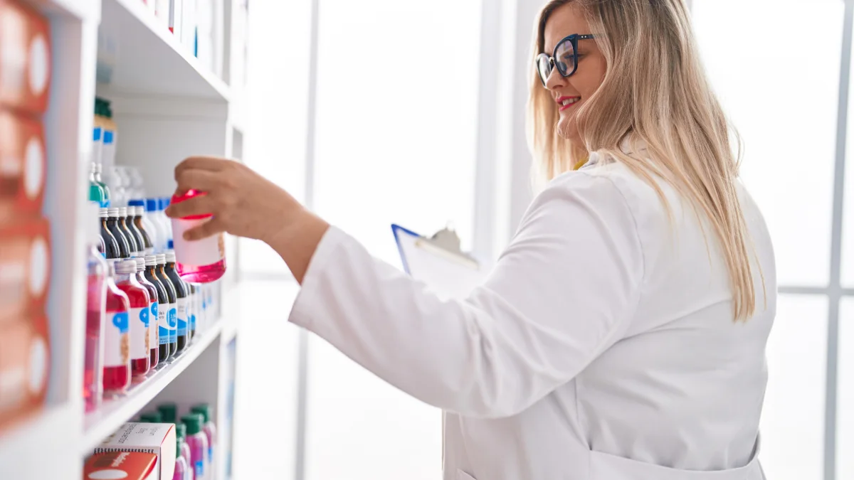Farmacêutica lendo um documento e segurando um frasco de medicamento